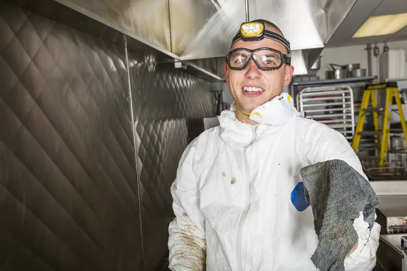 Technician scrubbing baked-on grease from stainless steel cooking equipment with a scrub pad