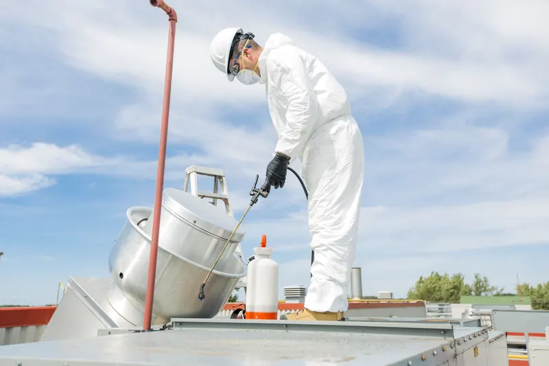 Technician on the roof of a food truck spraying degreaser on the exhaust fan