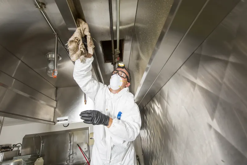 Technician wiping grease from the plenum chamber behind the filter bank of a stainless steel kitchen exhaust hood
